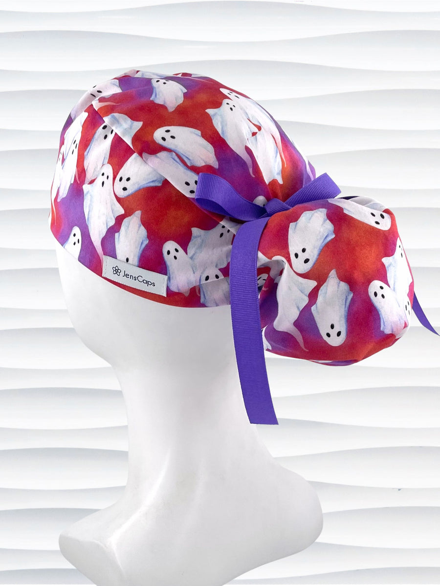 Ponytail style surgical scrub cap by JensCaps with white sheet ghosts tossed all aver an ombre red and purple cotton fabric.