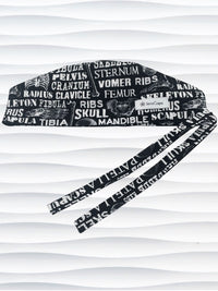 Anatomy-themed surgical scrub cap for medical professionals, featuring detailed white illustrations of the human skeleton with labeled bones like skull, mandible, and tibia on a black background
