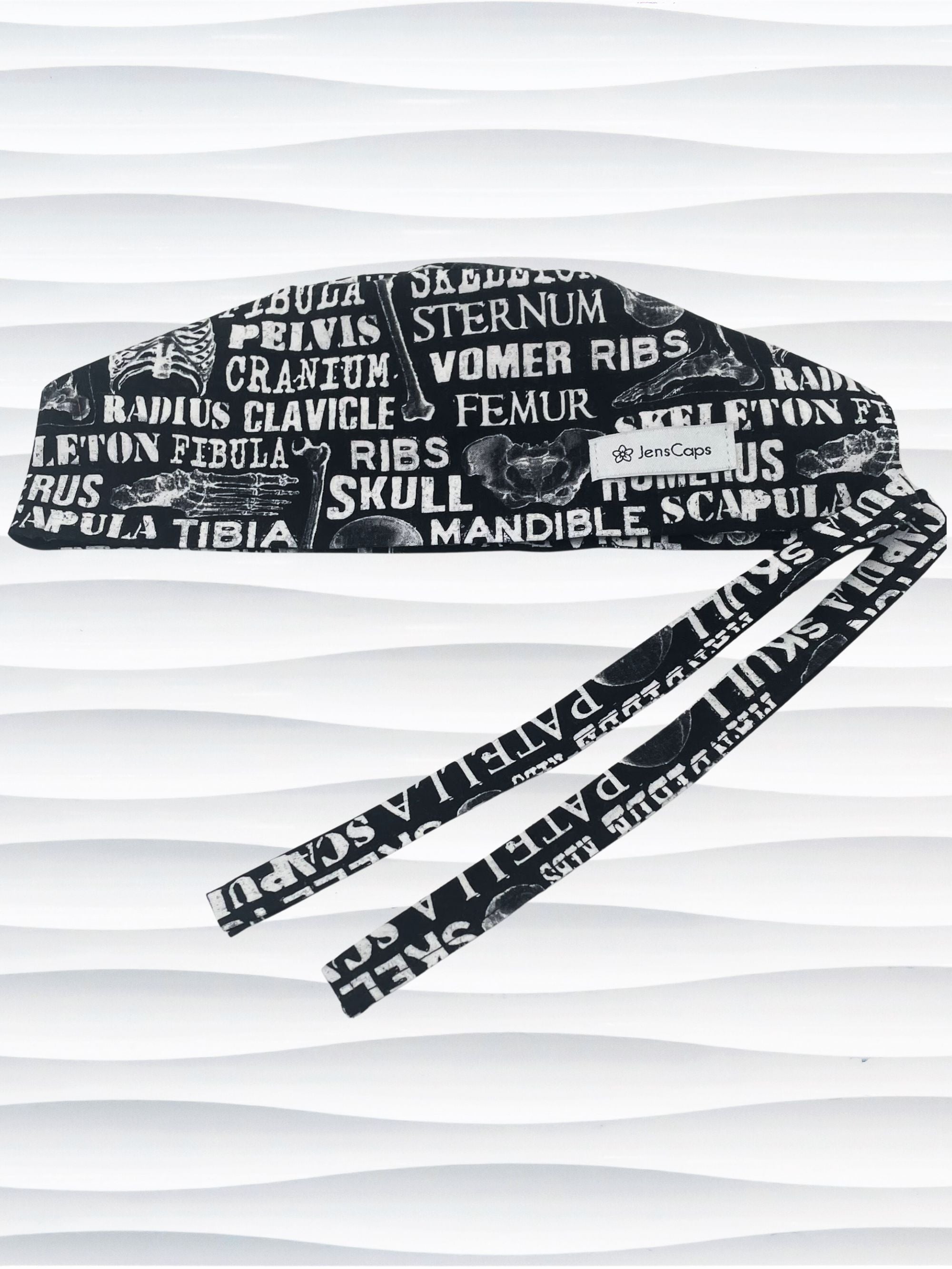 Anatomy-themed surgical scrub cap for medical professionals, featuring detailed white illustrations of the human skeleton with labeled bones like skull, mandible, and tibia on a black background