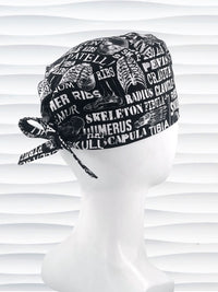 Anatomy-themed surgical scrub cap for medical professionals, featuring detailed white illustrations of the human skeleton with labeled bones like skull, mandible, and tibia on a black background