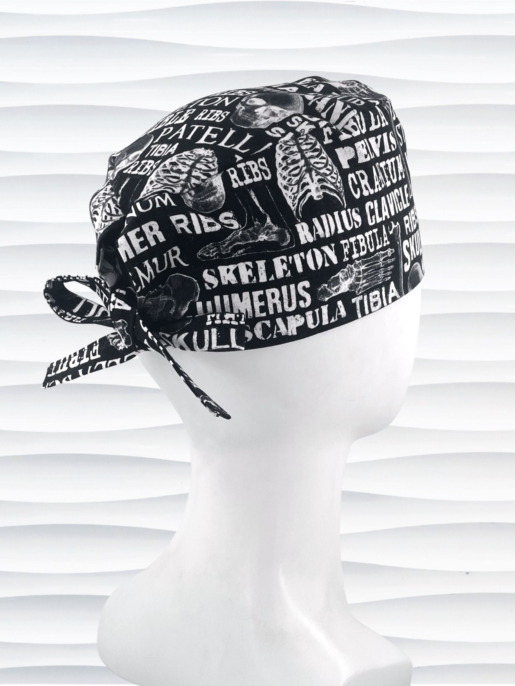 Anatomy-themed surgical scrub cap for medical professionals, featuring detailed white illustrations of the human skeleton with labeled bones like skull, mandible, and tibia on a black background