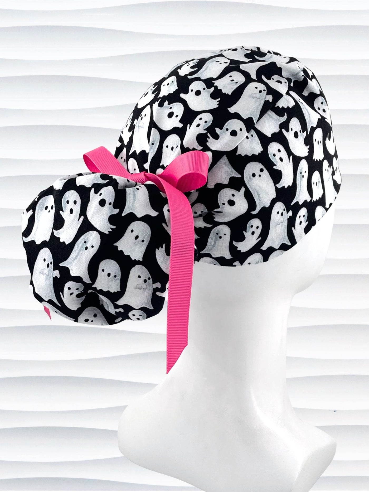 Ponytail style surgical scrub cap with animated white ghosts tossed all over black cotton fabric and finished with grosgrain ribbon ties.