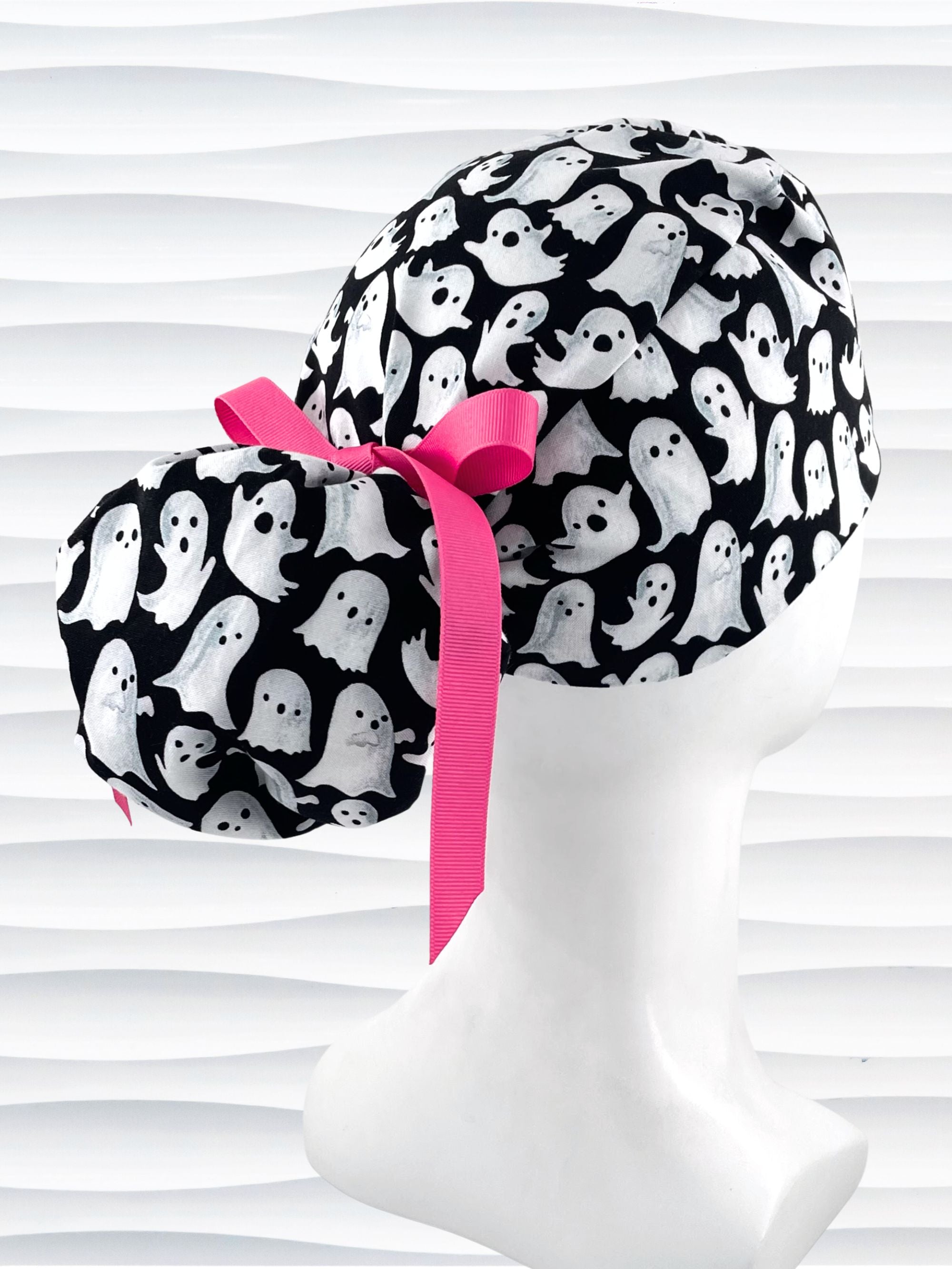 Ponytail style surgical scrub cap with animated white ghosts tossed all over black cotton fabric and finished with grosgrain ribbon ties.