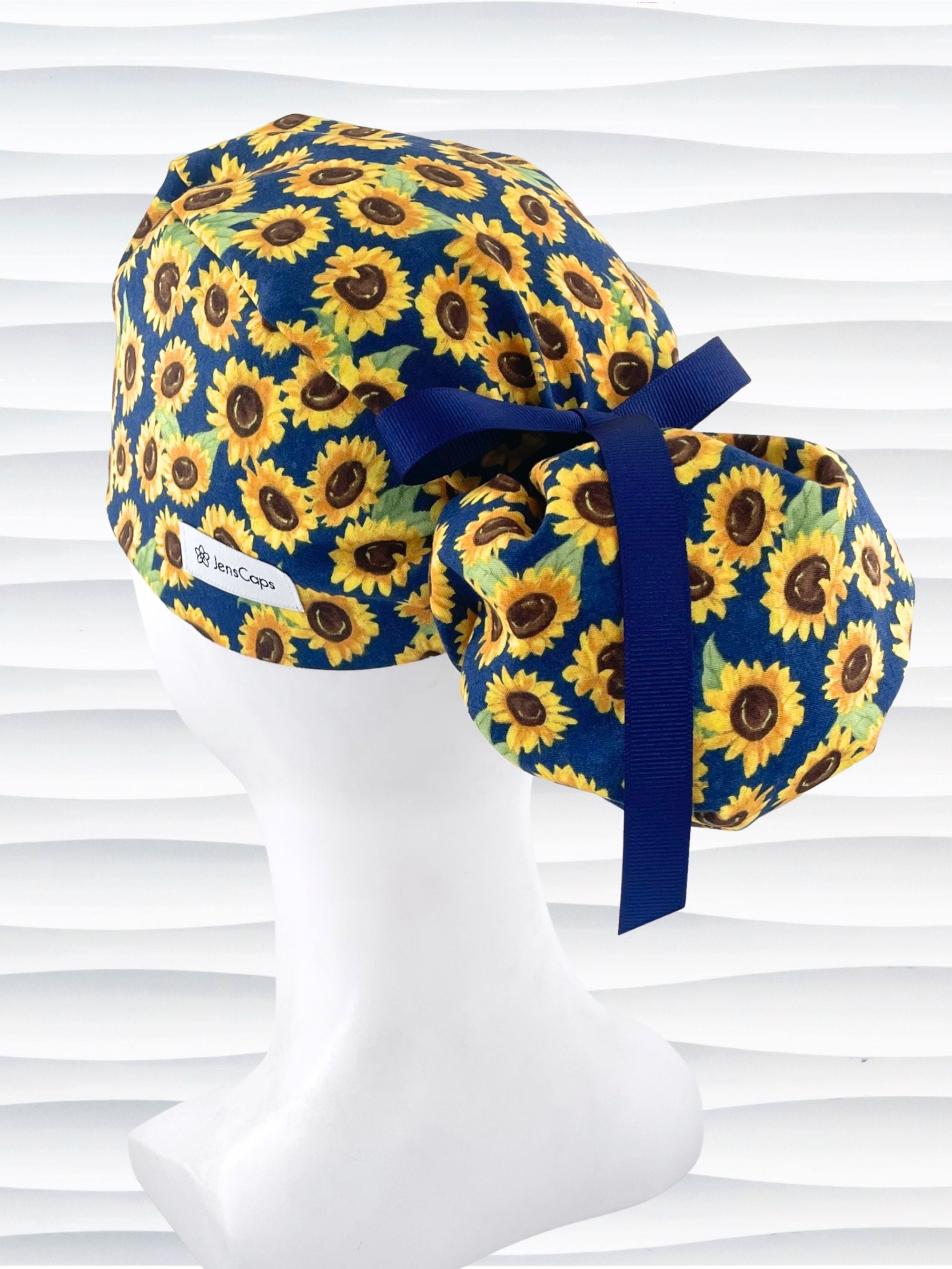 Ponytail style surgical scrub cap by jenscaps with sunflowers tossed all over a dark blue background cotton fabric and finished with ribbon ties.