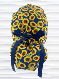 Ponytail style surgical scrub cap by jenscaps with sunflowers tossed all over a dark blue background cotton fabric and finished with ribbon ties.