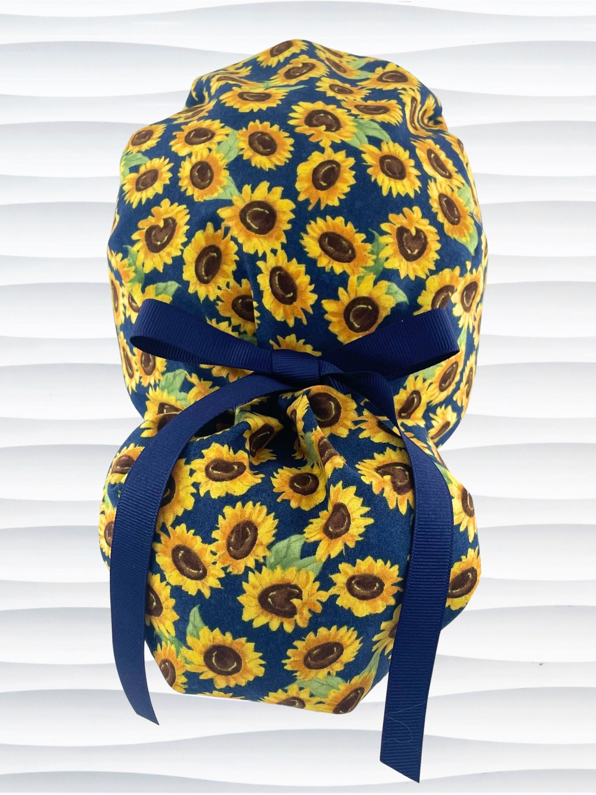 Ponytail style surgical scrub cap by jenscaps with sunflowers tossed all over a dark blue background cotton fabric and finished with ribbon ties.