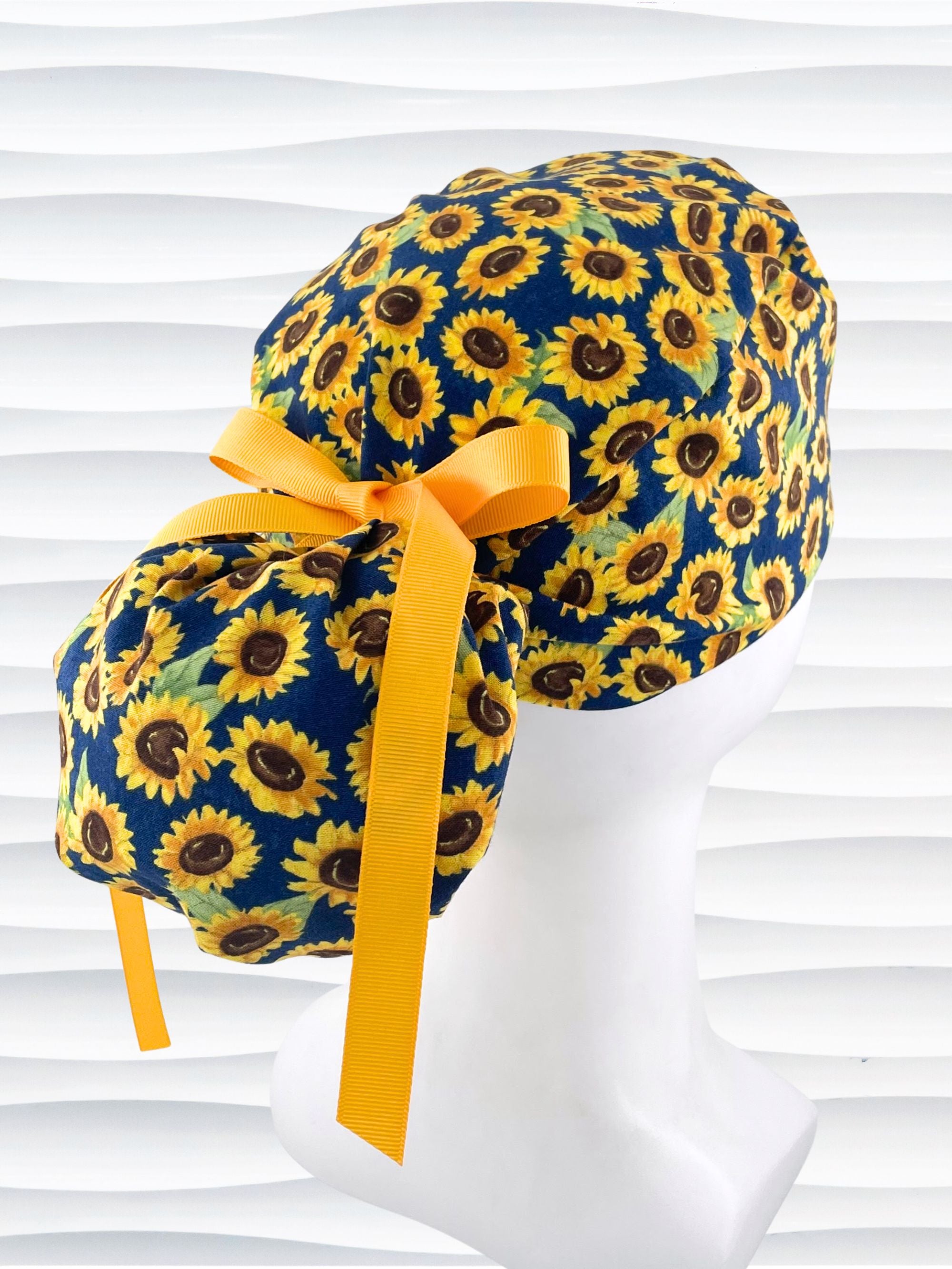 Ponytail style surgical scrub cap by jenscaps with sunflowers tossed all over a dark blue background cotton fabric and finished with ribbon ties.
