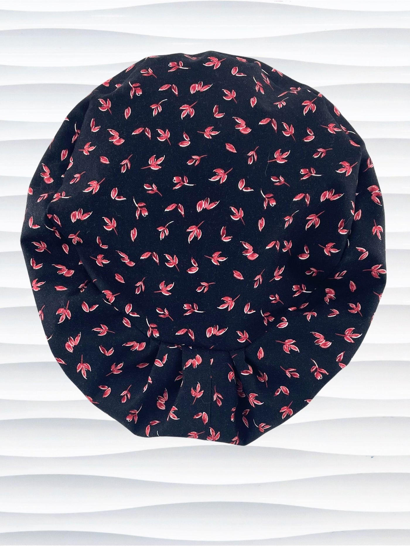 Black scrub cap with pink floral pattern on a mannequin head against a white background