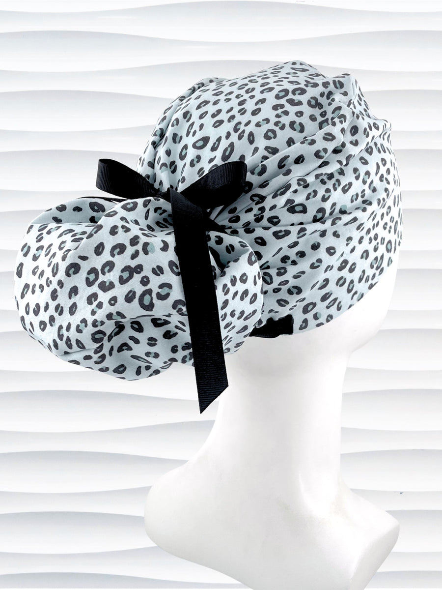 Euro Pony style surgical scrub cap by JensCaps with a leopard print on light teal cotton fabric, tied with a ribbon, and displayed on a mannequin head.