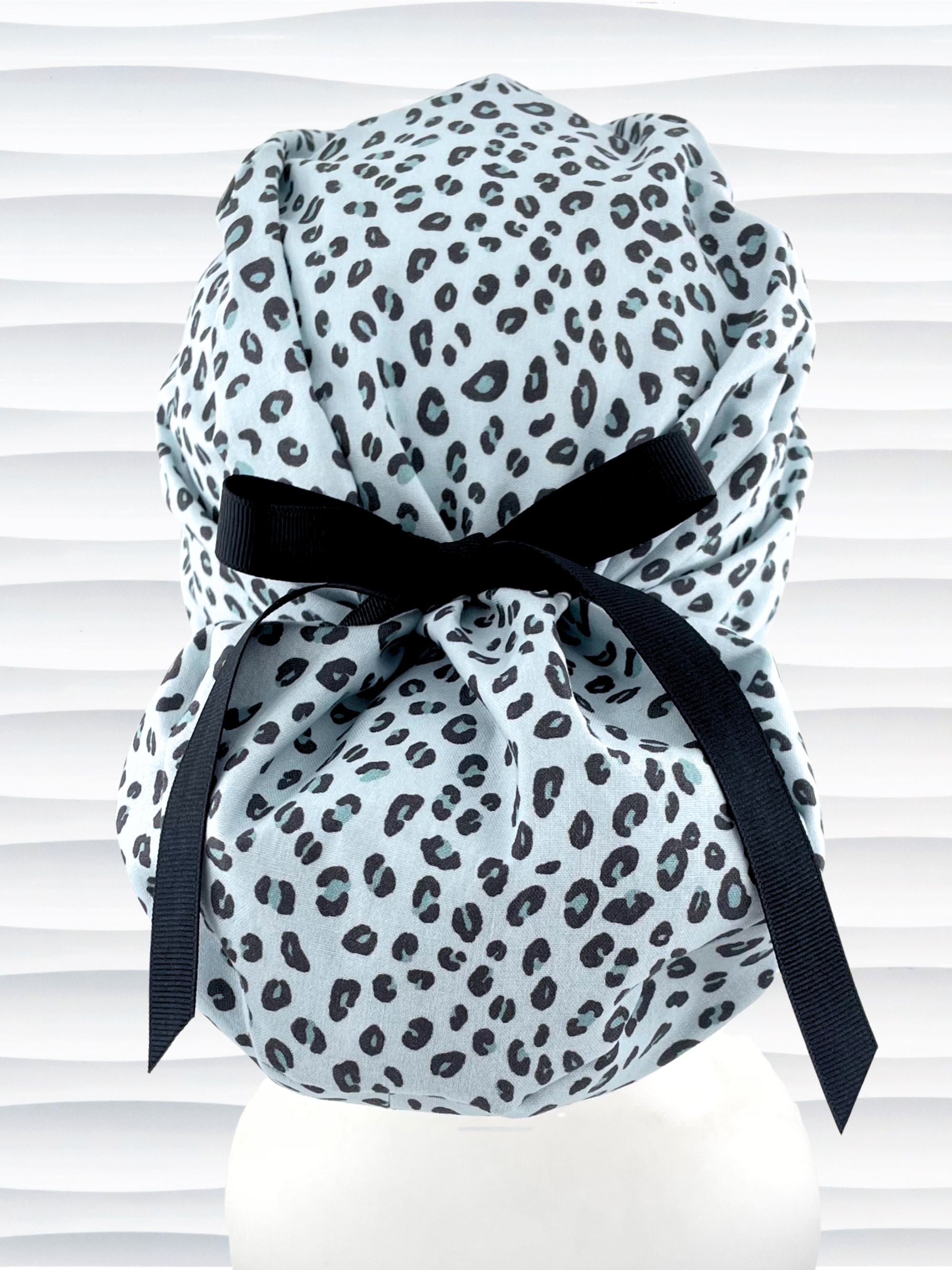 Euro Pony style surgical scrub cap by JensCaps with a leopard print on light teal cotton fabric, tied with a ribbon, and displayed on a mannequin head.