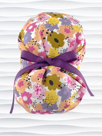 Euro Pony style surgical scrub cap by JensCaps with pink, purple, yellow, and green flowers all over white cotton fabric, tied with a ribbon and displayed on a mannequin head.