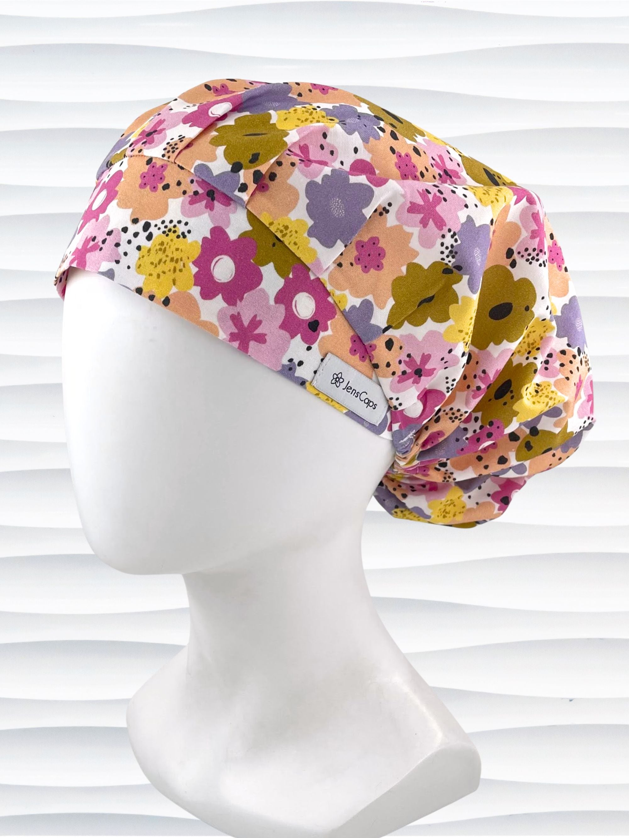 Bouffant style surgical scrub cap by JensCaps with pink, purple, yellow, and green flowers all over white cotton fabric  and displayed on a mannequin head.