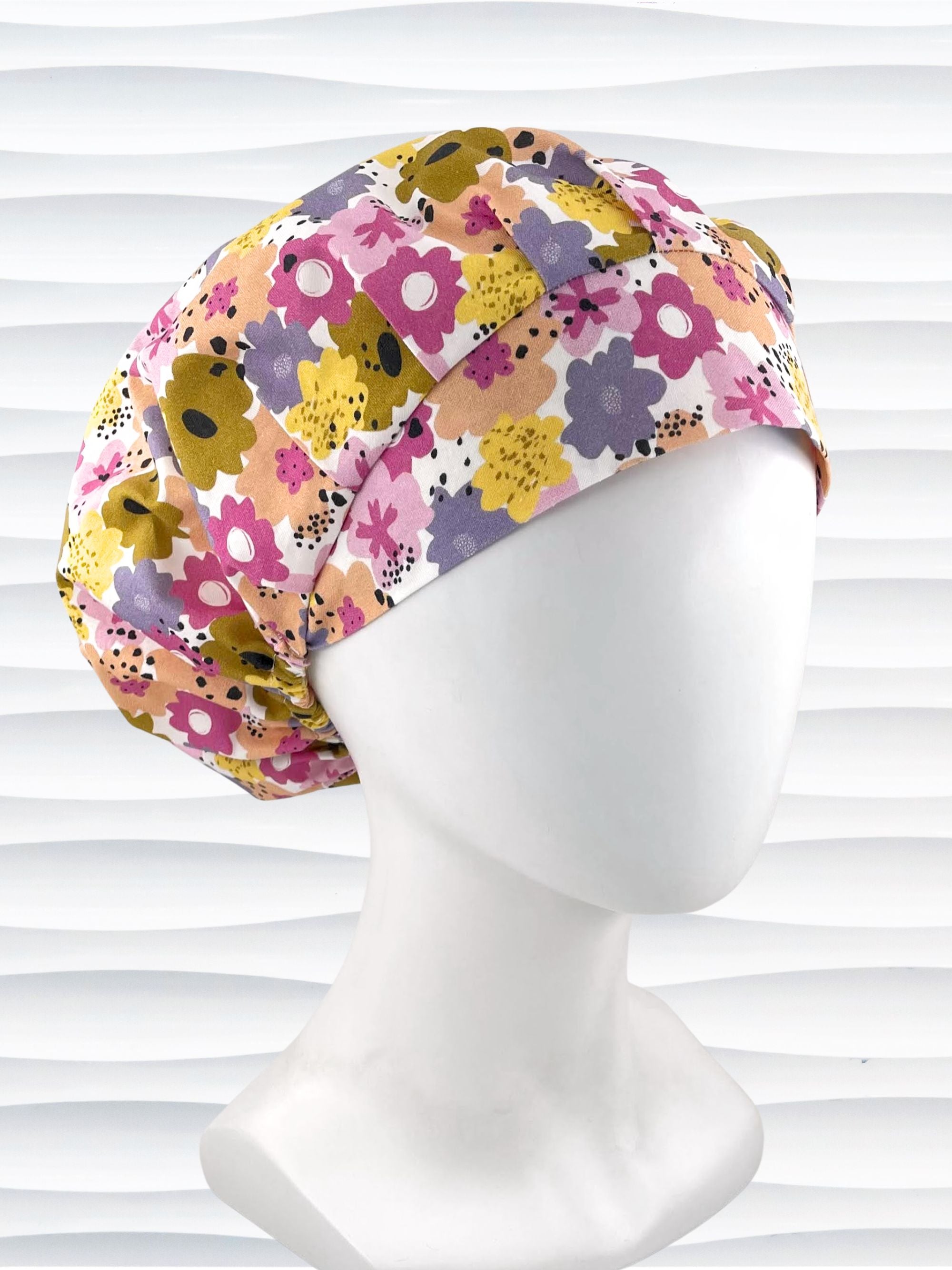 Bouffant style surgical scrub cap by JensCaps with pink, purple, yellow, and green flowers all over white cotton fabric  and displayed on a mannequin head.