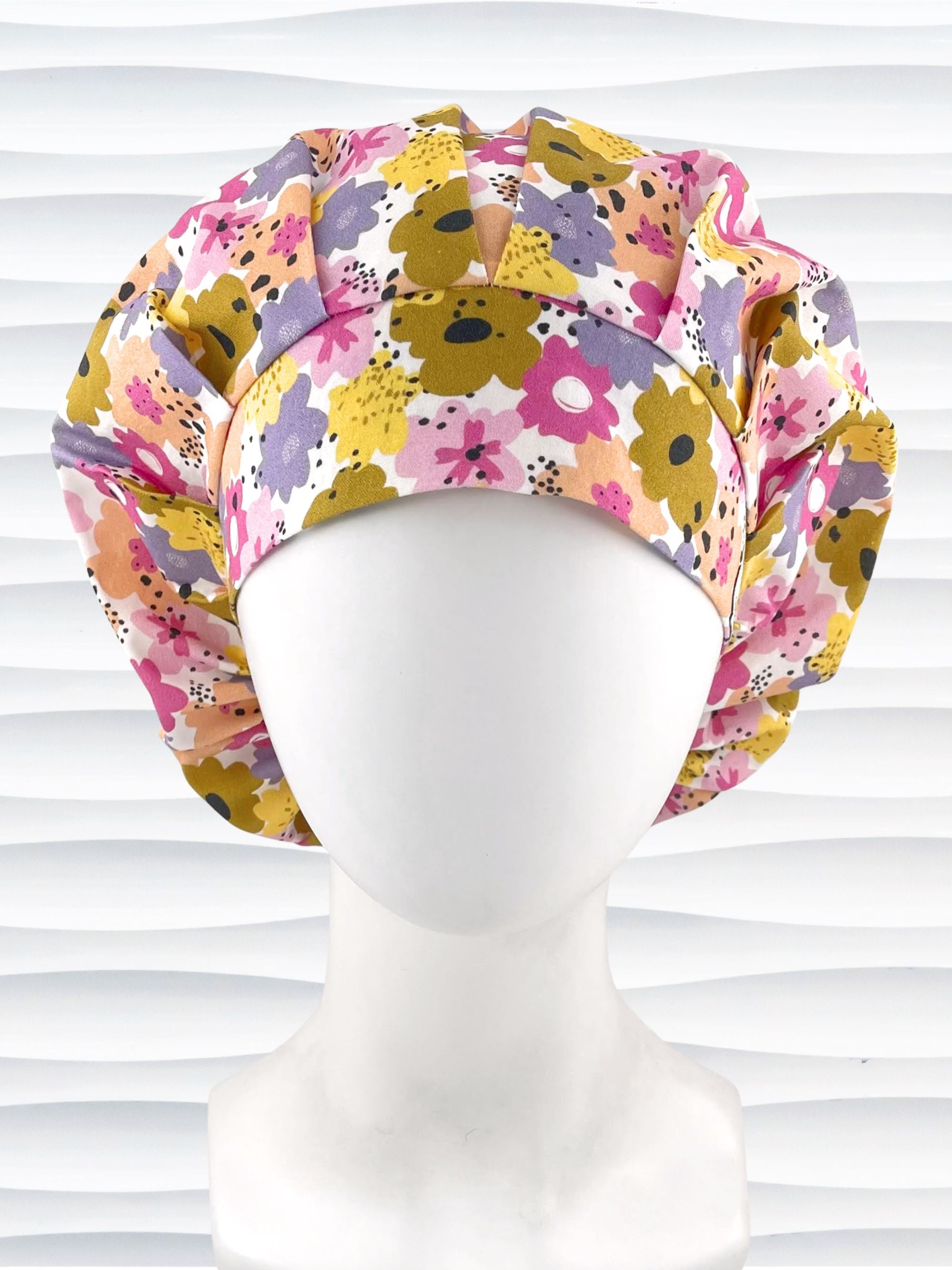 Bouffant style surgical scrub cap by JensCaps with pink, purple, yellow, and green flowers all over white cotton fabric  and displayed on a mannequin head.