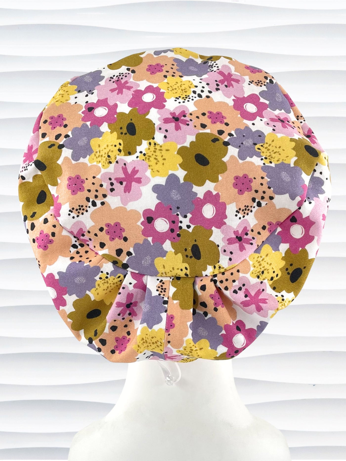 Euro Pixie style surgical scrub cap by JensCaps with pink, purple, yellow, and green flowers all over white cotton fabric  and displayed on a mannequin head.