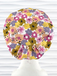 Euro Pixie style surgical scrub cap by JensCaps with pink, purple, yellow, and green flowers all over white cotton fabric  and displayed on a mannequin head.