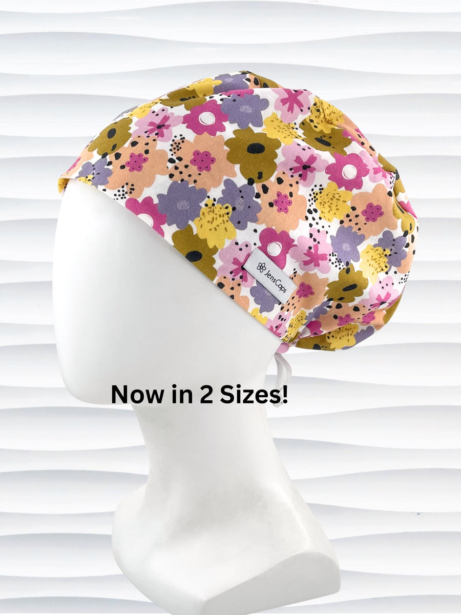 Euro Pixie style surgical scrub cap by JensCaps with pink, purple, yellow, and green flowers all over white cotton fabric  and displayed on a mannequin head.