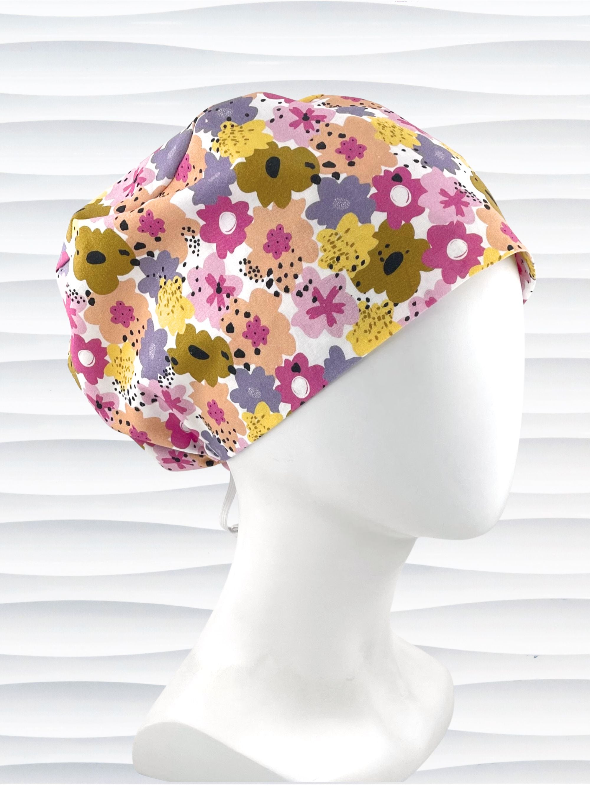Euro Pixie style surgical scrub cap by JensCaps with pink, purple, yellow, and green flowers all over white cotton fabric  and displayed on a mannequin head.