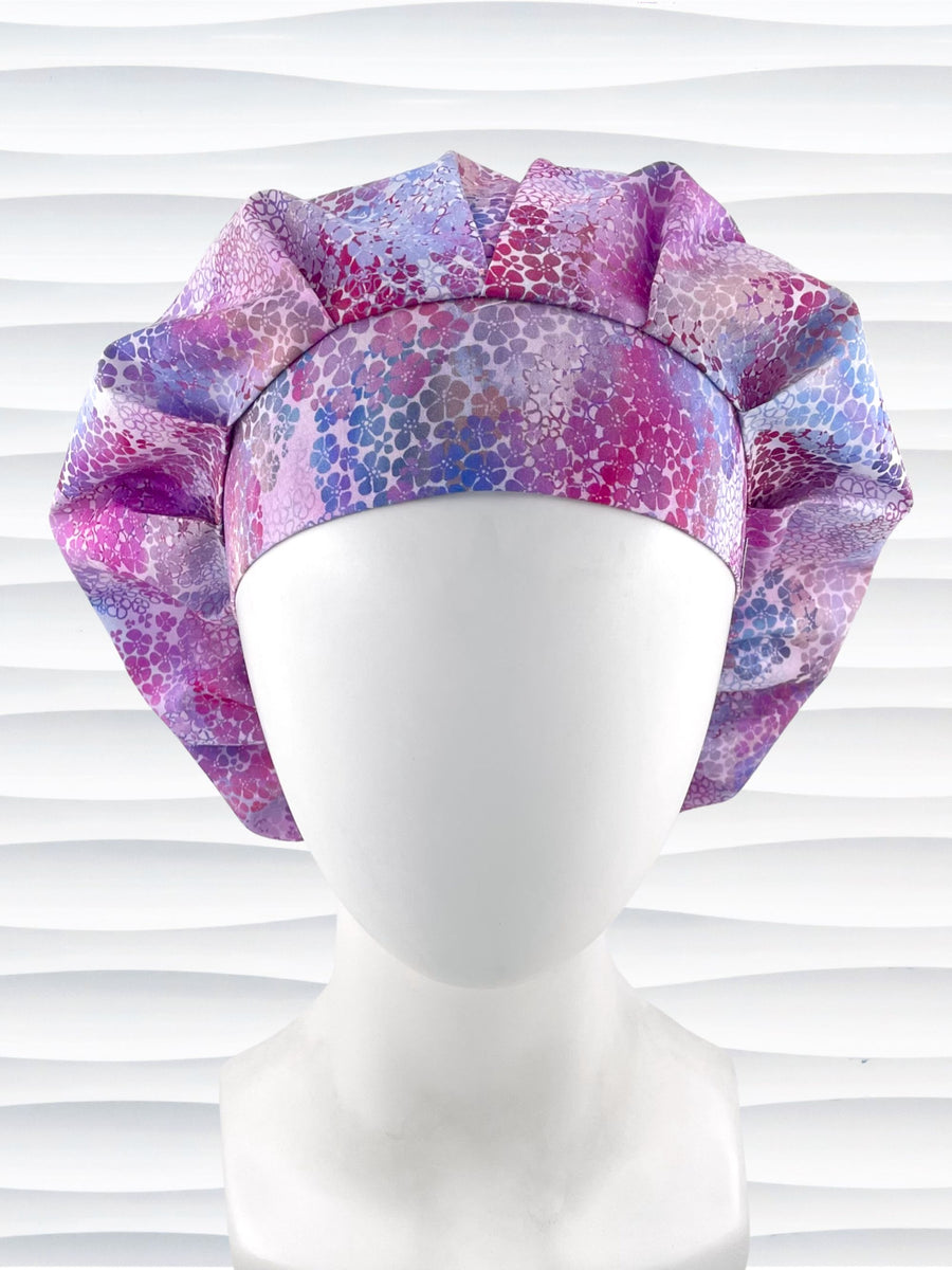 Bouffant style surgical scrub cap by JensCaps with small daisies in pink, blue, and purple all over cotton fabric and displayed on a mannequin head