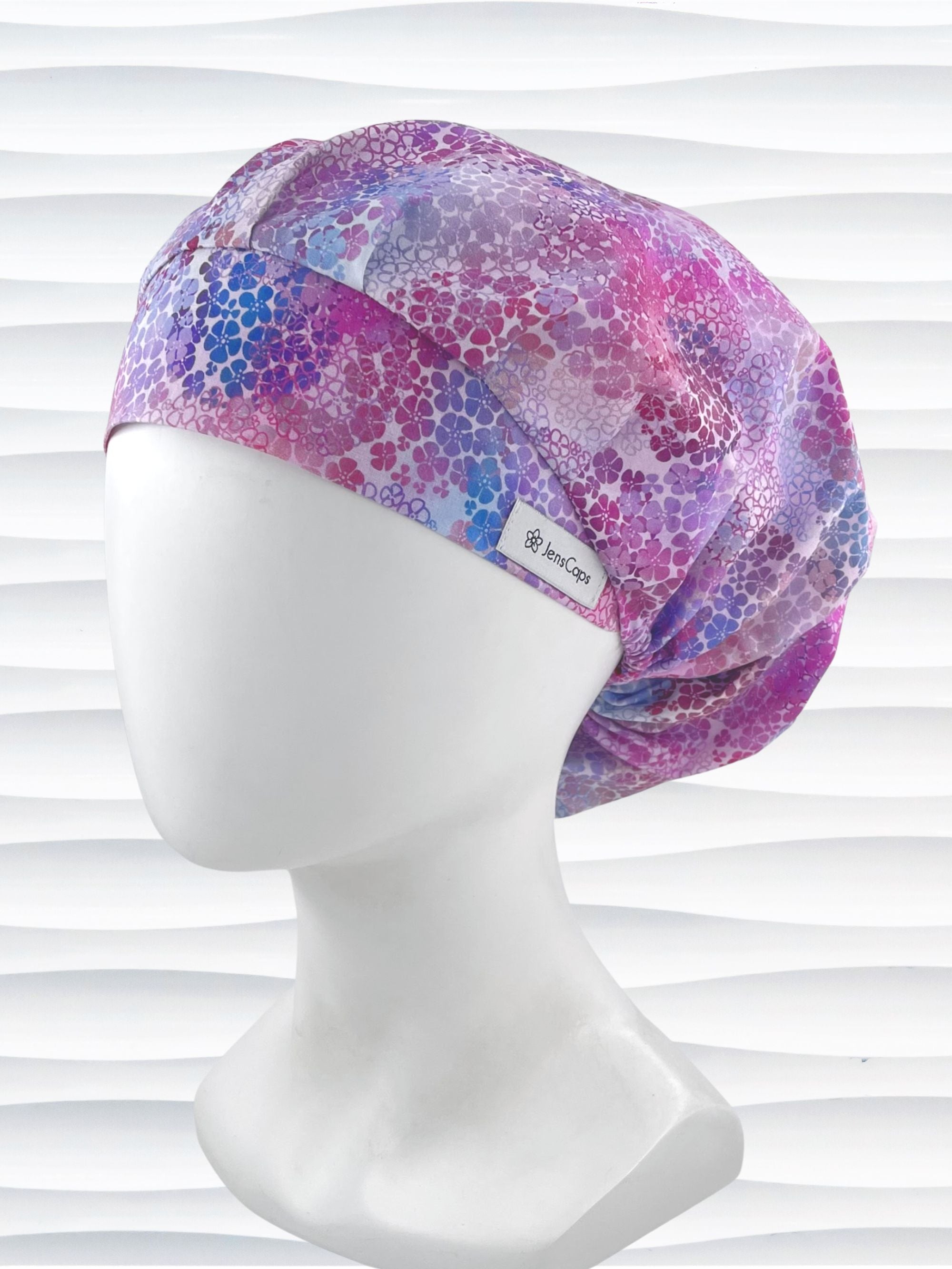 Bouffant style surgical scrub cap by JensCaps with small daisies in pink, blue, and purple all over cotton fabric and displayed on a mannequin head