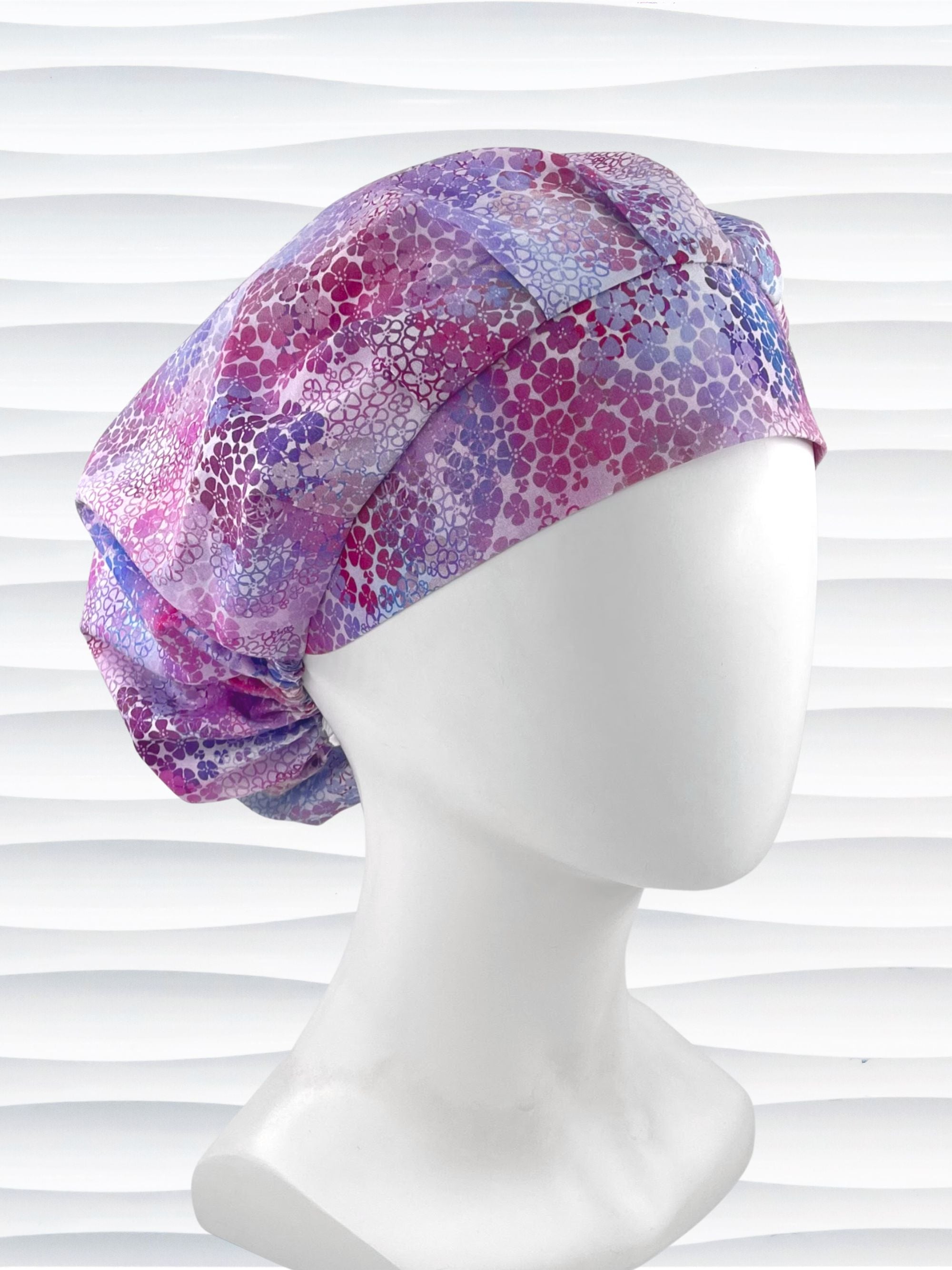 Bouffant style surgical scrub cap by JensCaps with small daisies in pink, blue, and purple all over cotton fabric and displayed on a mannequin head