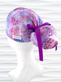 Ponytail style surgical scrub cap by JensCaps with small daisies in pink, blue, and purple all over cotton fabric, tied with a ribbon, and displayed on a mannequin head