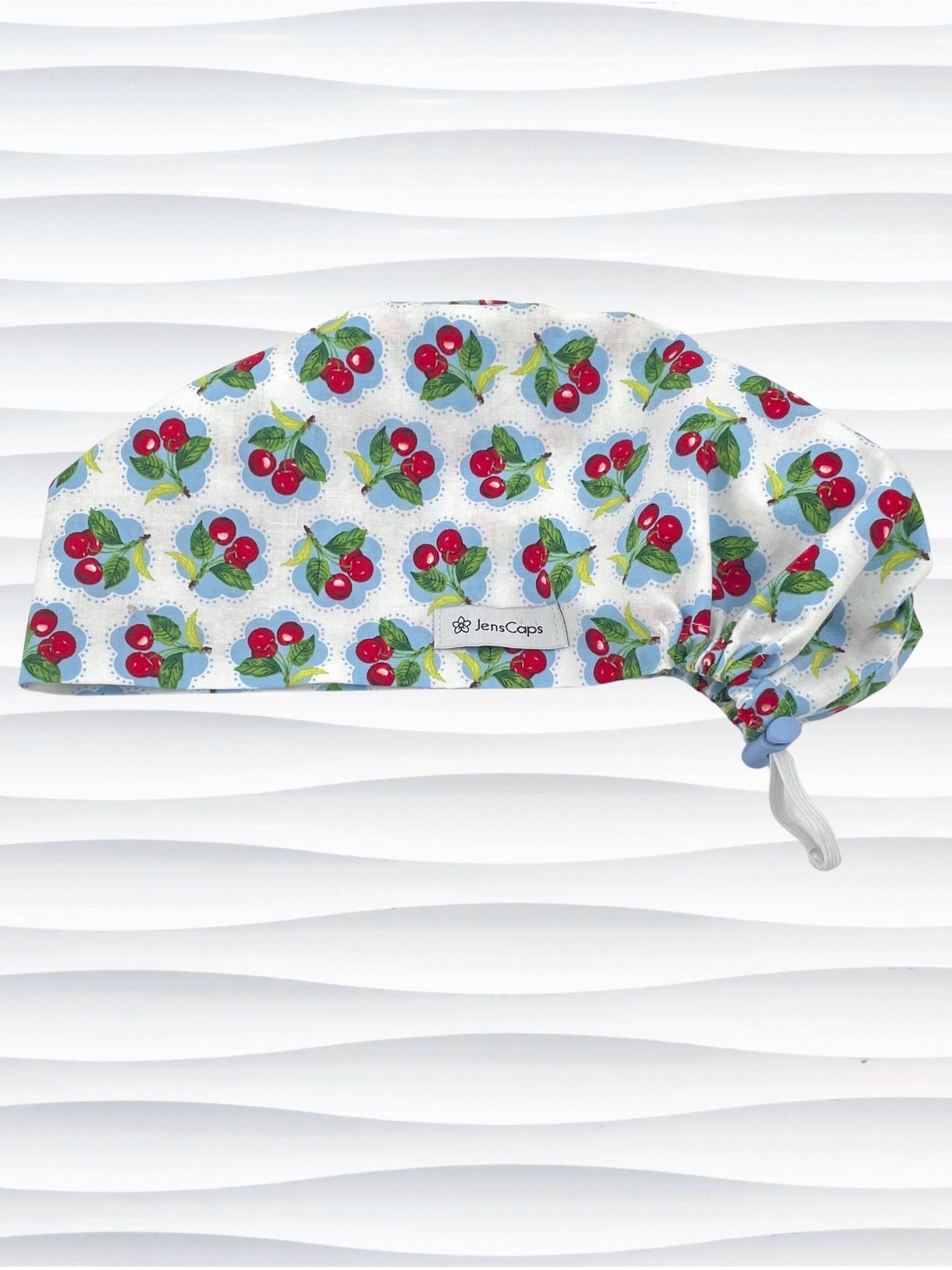 Euro Pixie style surgical scrub cap by JensCaps with red cherries blue polka dots on white cotton fabric and diplayed on a mannequin head.