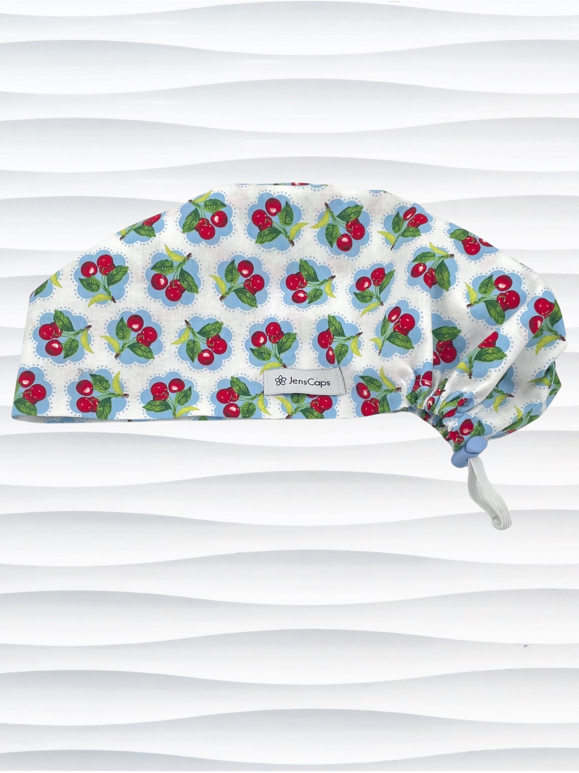 Euro Pixie style surgical scrub cap by JensCaps with red cherries blue polka dots on white cotton fabric and diplayed on a mannequin head.