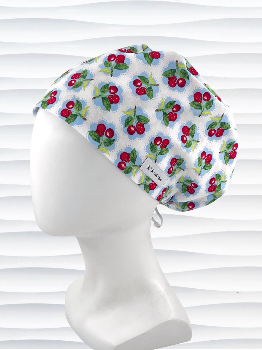 Euro Pixie style surgical scrub cap by JensCaps with red cherries blue polka dots on white cotton fabric and diplayed on a mannequin head.