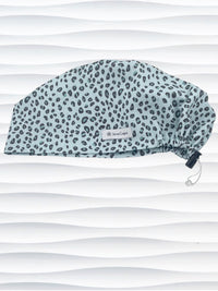 Euro Pixie style surgical scrub cap by JensCaps with a leopard print on light teal cotton fabric and displayed on a mannequin head.