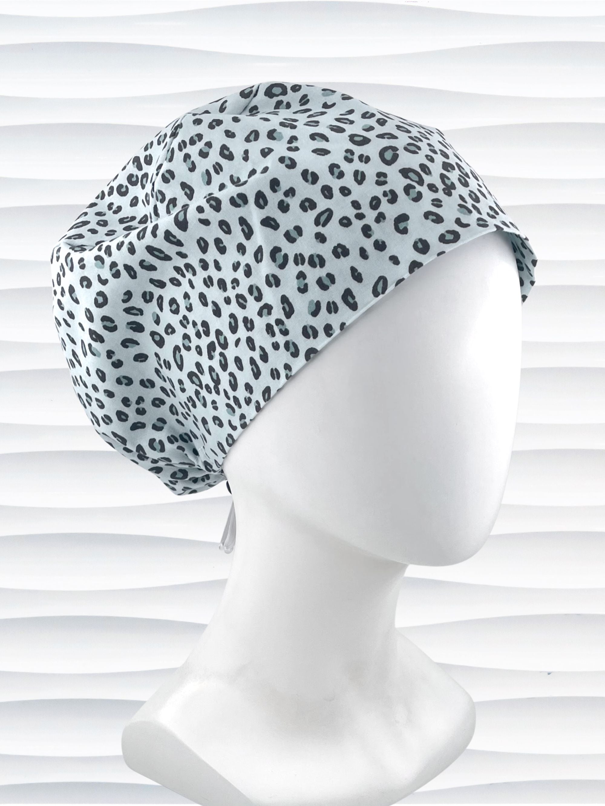 Euro Pixie style surgical scrub cap by JensCaps with a leopard print on light teal cotton fabric and displayed on a mannequin head.