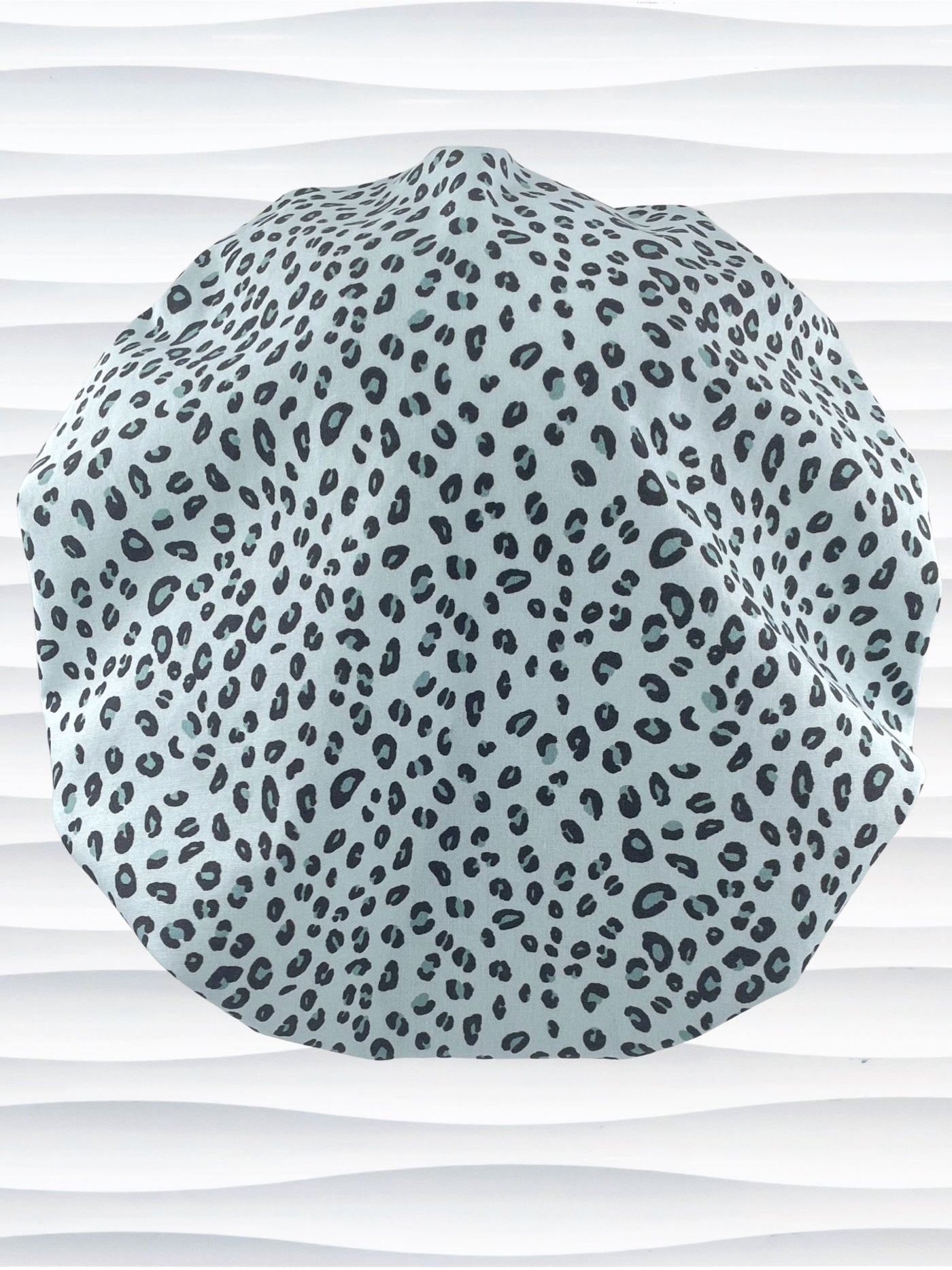 Bouffant style surgical scrub cap by JensCaps with a leopard print on light teal cotton fabric, and displayed on a mannequin head.