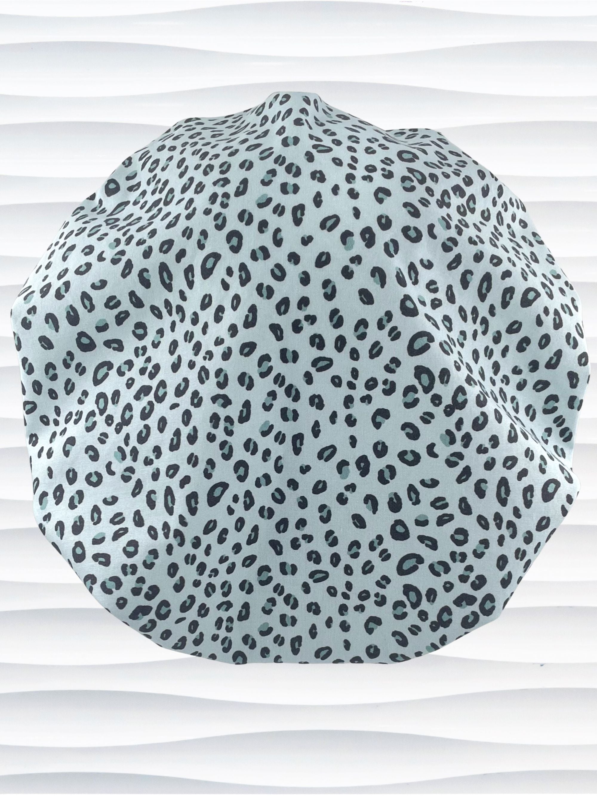 Bouffant style surgical scrub cap by JensCaps with a leopard print on light teal cotton fabric, and displayed on a mannequin head.