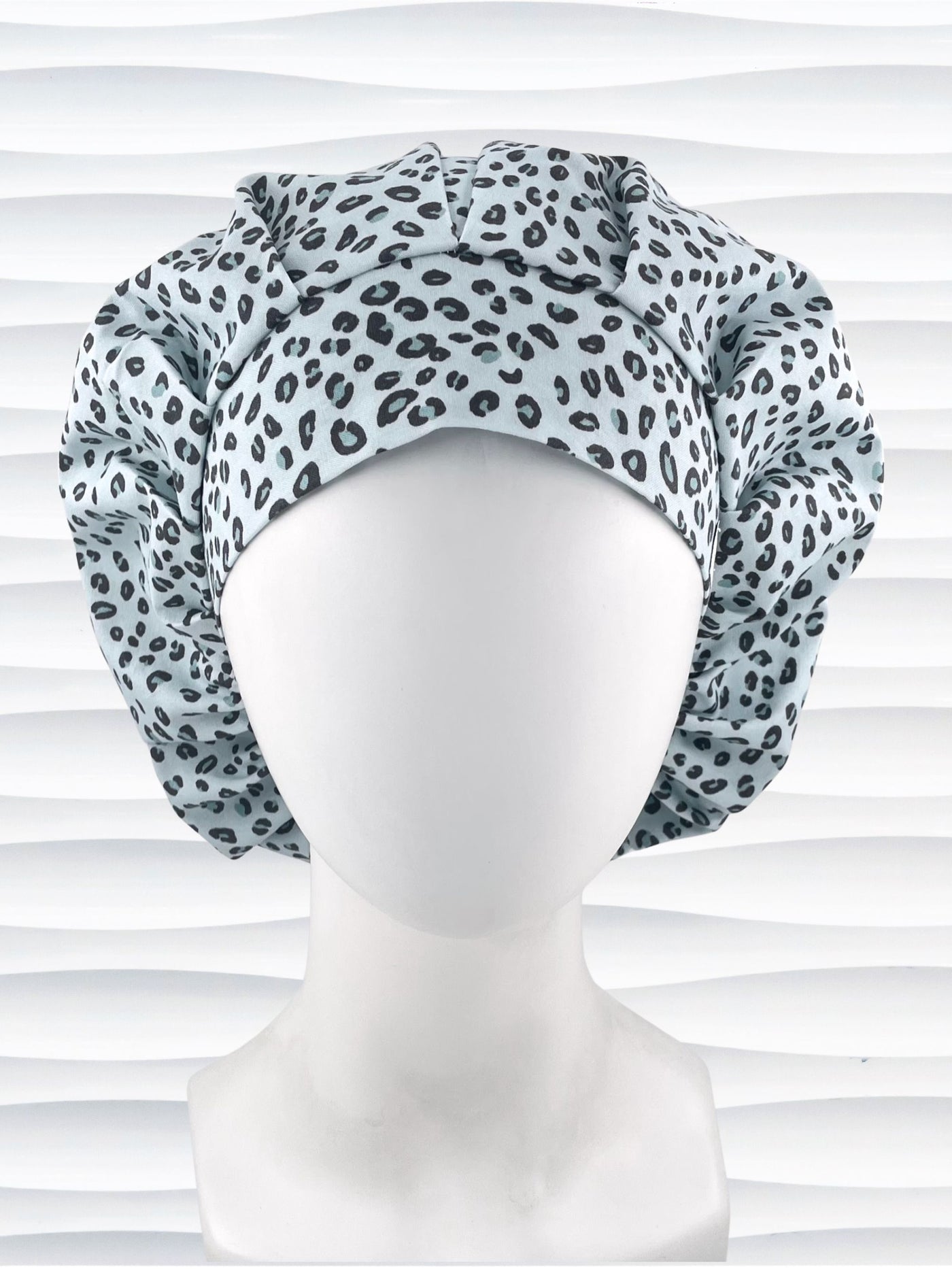 Bouffant style surgical scrub cap by JensCaps with a leopard print on light teal cotton fabric, and displayed on a mannequin head.