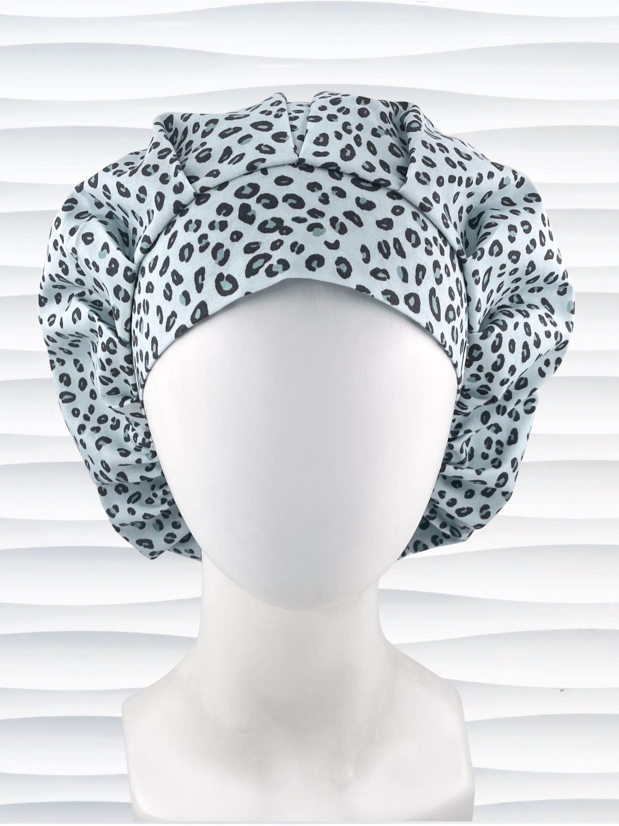 Bouffant style surgical scrub cap by JensCaps with a leopard print on light teal cotton fabric, and displayed on a mannequin head.