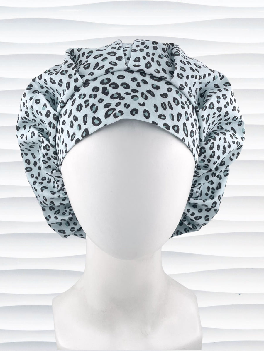 Bouffant style surgical scrub cap by JensCaps with a leopard print on light teal cotton fabric, and displayed on a mannequin head.