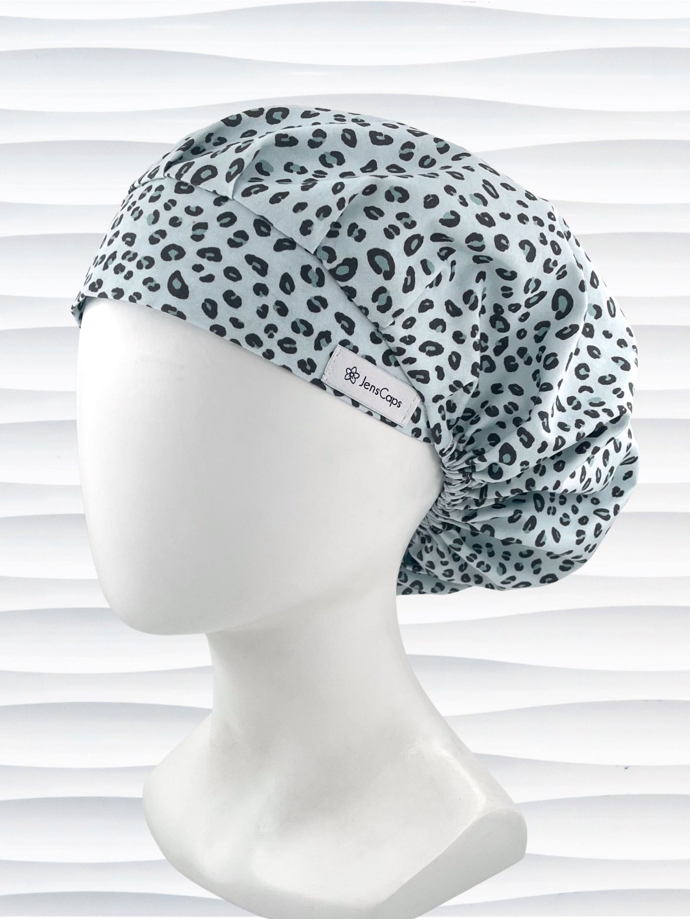 Bouffant style surgical scrub cap by JensCaps with a leopard print on light teal cotton fabric, and displayed on a mannequin head.