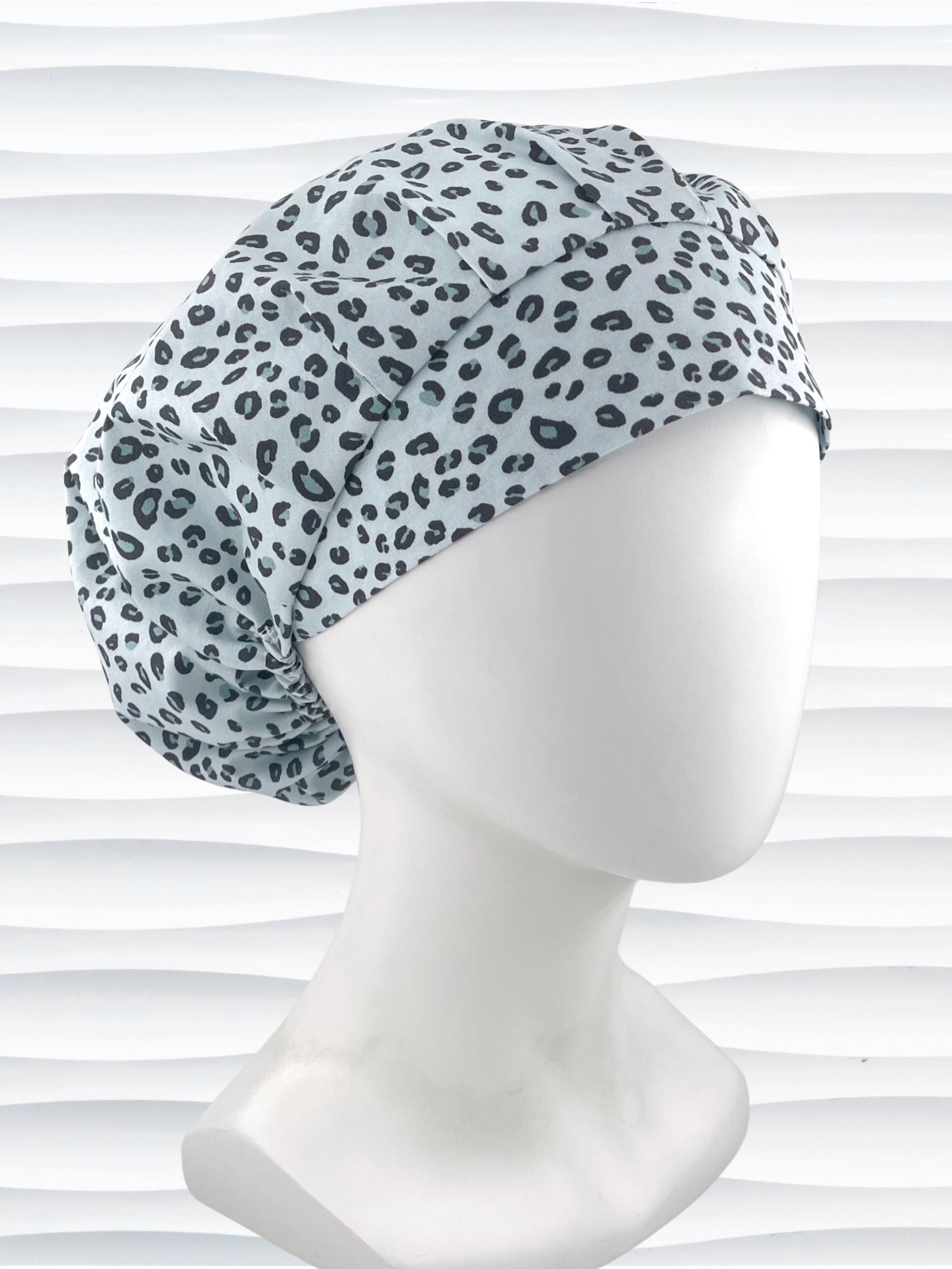 Bouffant style surgical scrub cap by JensCaps with a leopard print on light teal cotton fabric, and displayed on a mannequin head.