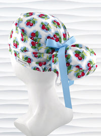 Euro Pony style surgical scrub cap by JensCaps with red cherries blue polka dots on white cotton fabric, finished with a ribbon tie, and displayed on a mannequin head.