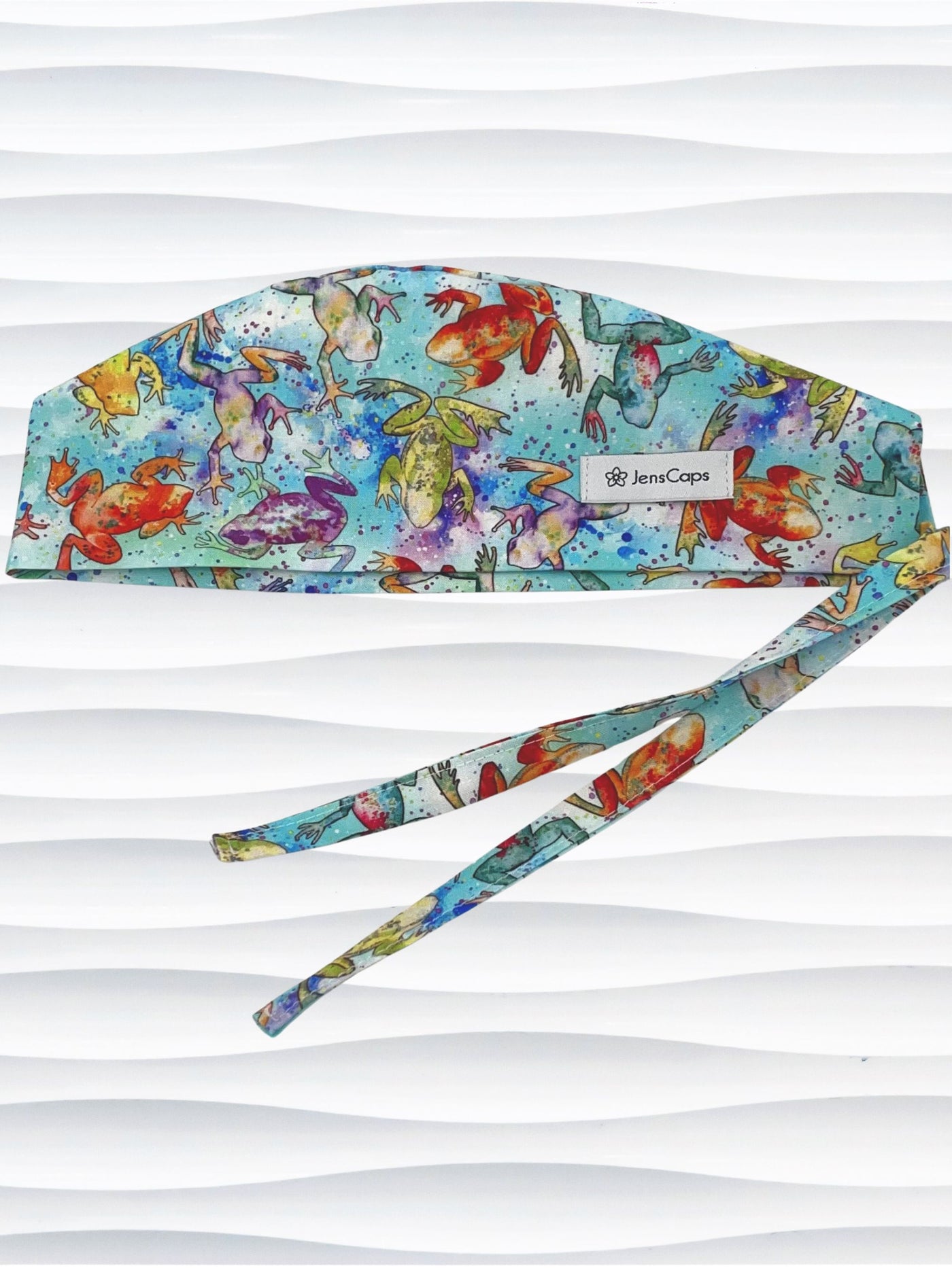 Surgical scrub cap by JensCaps in an adjustable tie-back style with a colorful watercolor frog print in orange, purple, green, and blue on an aqua background