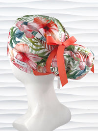 Euro Pony style surgical scrub cap by JensCaps with tropical hibiscus flowers and palm fronds all over white cotton fabric, finished with a grosgrain ribbon tie, and displayed on a mannequin head