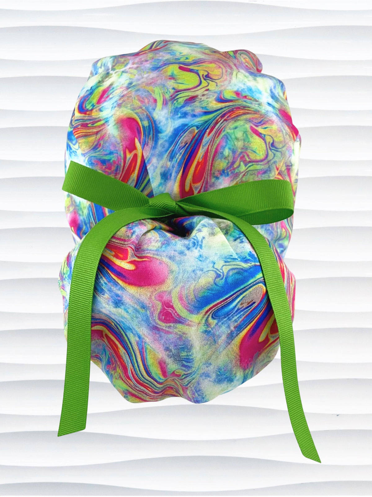 Ponytail style surgical scrub cap by JensCaps with an abstract marbled swirl print in blue, pink, yellow, and green, finished with a grosgrain ribbon, and displayed on a white mannequin head.