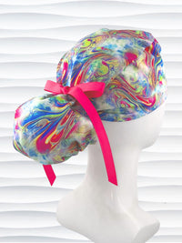 Ponytail style surgical scrub cap by JensCaps with an abstract marbled swirl print in blue, pink, yellow, and green, finished with a grosgrain ribbon, and displayed on a white mannequin head.