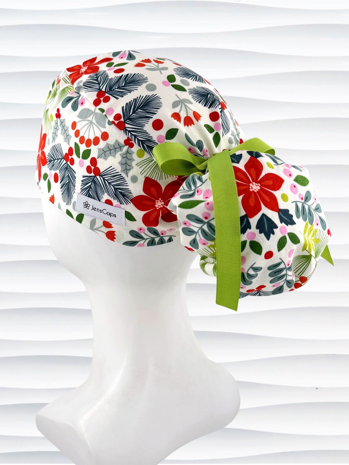 Ponytail style surgical scrub cap by jenscaps with holly berries, mistletoe, and poinsettias all over this white cotton fabric and tied with a ribbon