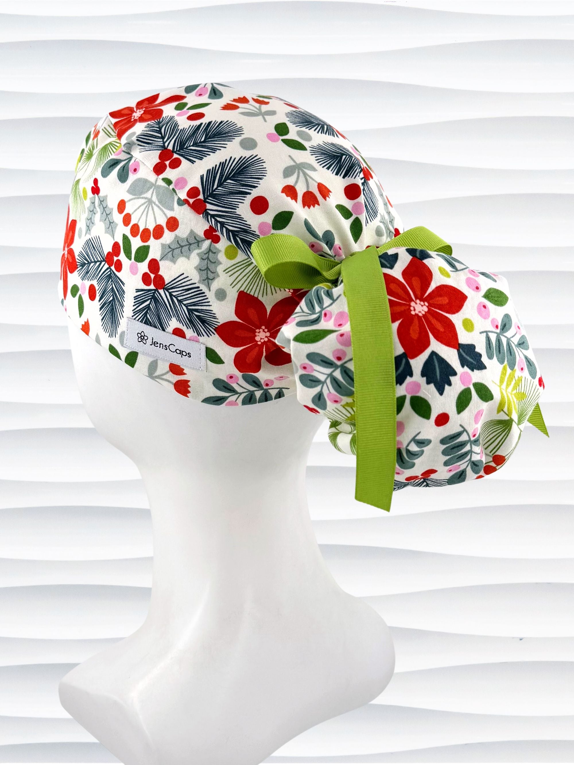 Ponytail style surgical scrub cap by jenscaps with holly berries, mistletoe, and poinsettias all over this white cotton fabric and tied with a ribbon