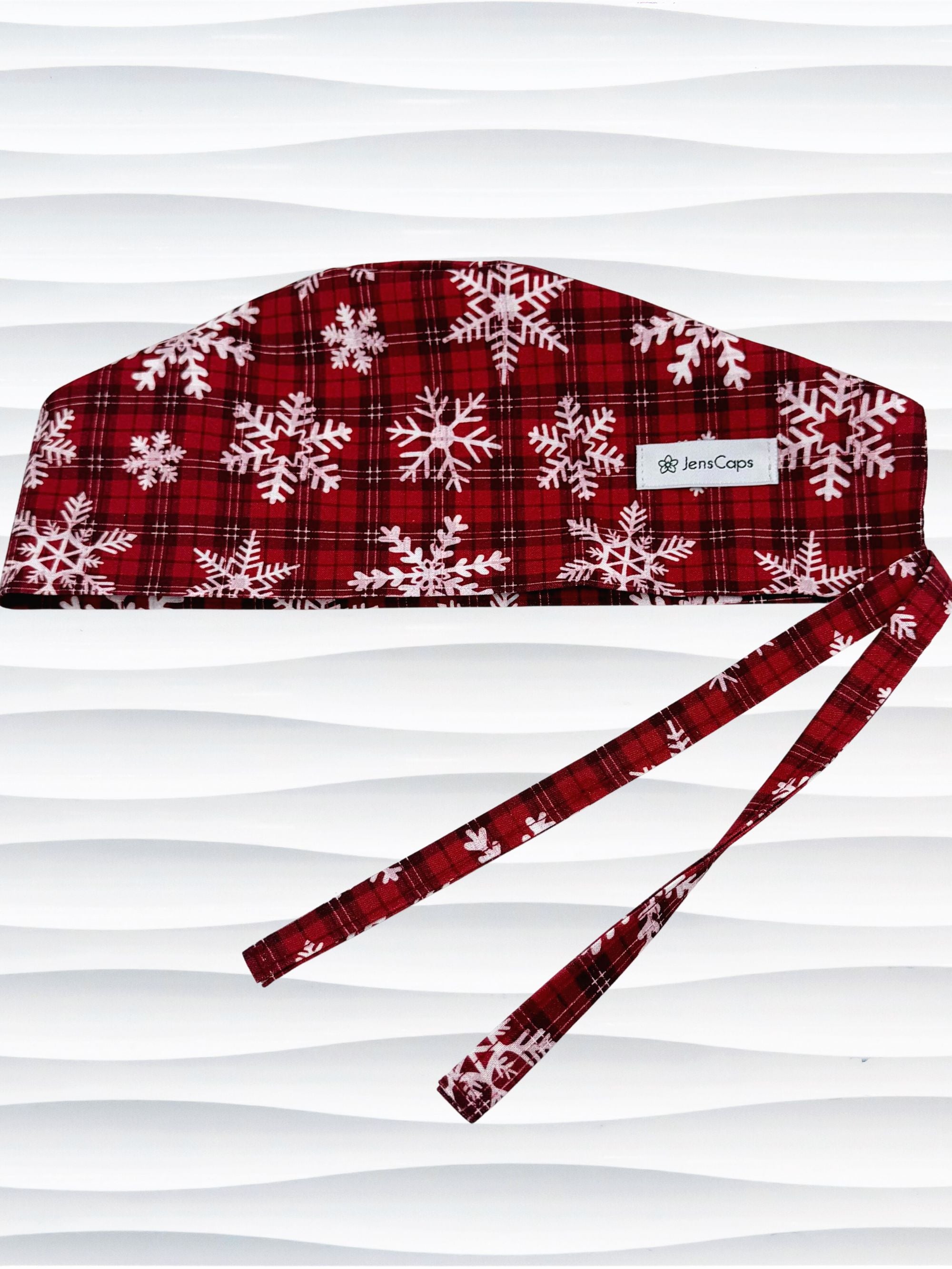 Red and white plaid scrub cap with snowflakes on a mannequin head against a white background.