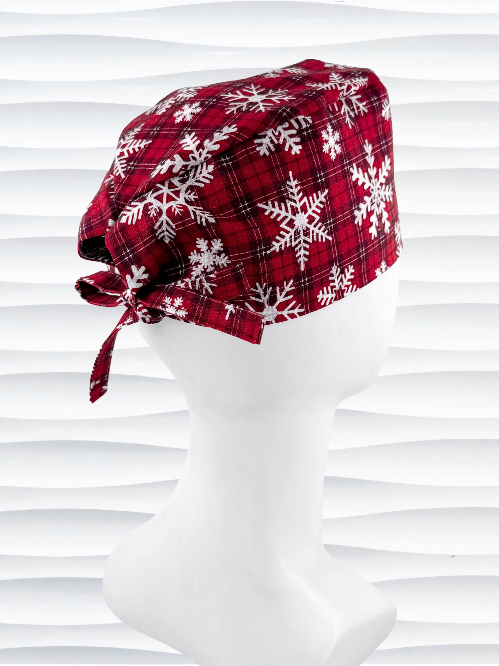 Red and white plaid scrub cap with snowflakes on a mannequin head against a white background.