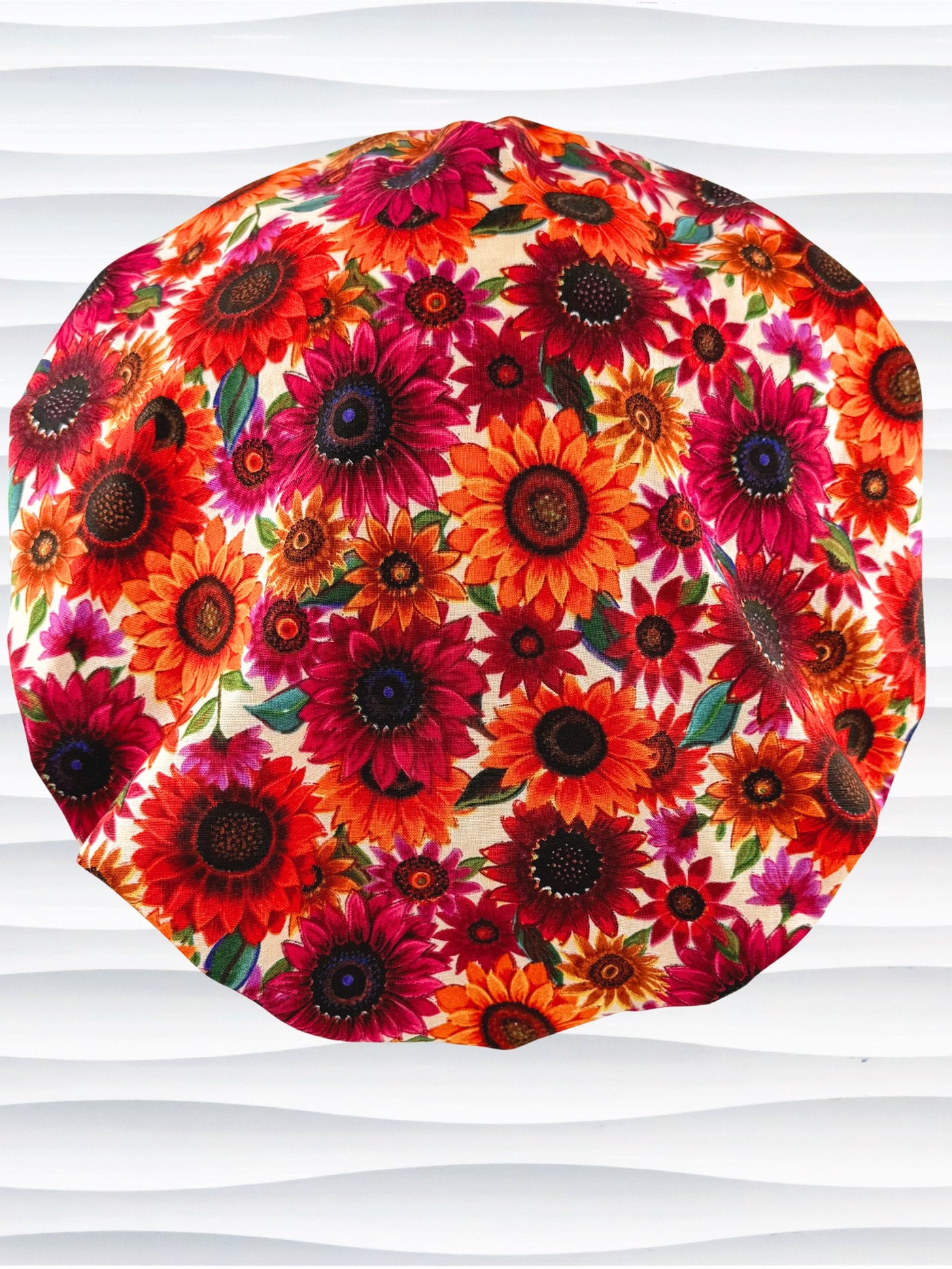 Bouffant surgical scrub cap by JensCaps with fall colored sunflowers in pinks, orange, and reds on a white background cotton fabric.