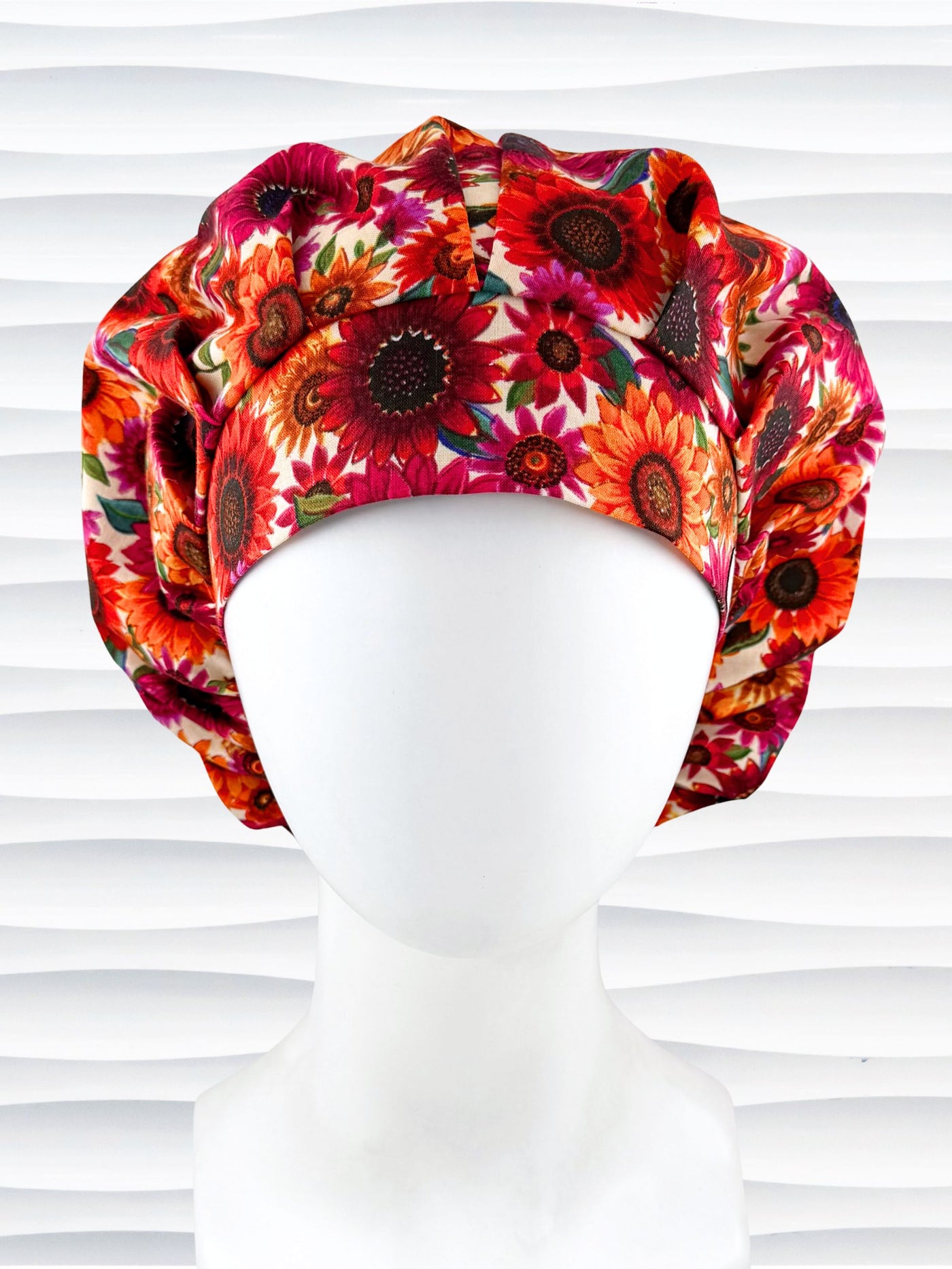 Bouffant surgical scrub cap by JensCaps with fall colored sunflowers in pinks, orange, and reds on a white background cotton fabric.