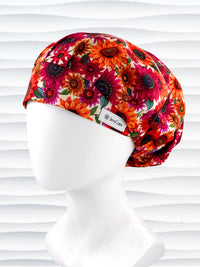 Bouffant surgical scrub cap by JensCaps with fall colored sunflowers in pinks, orange, and reds on a white background cotton fabric.